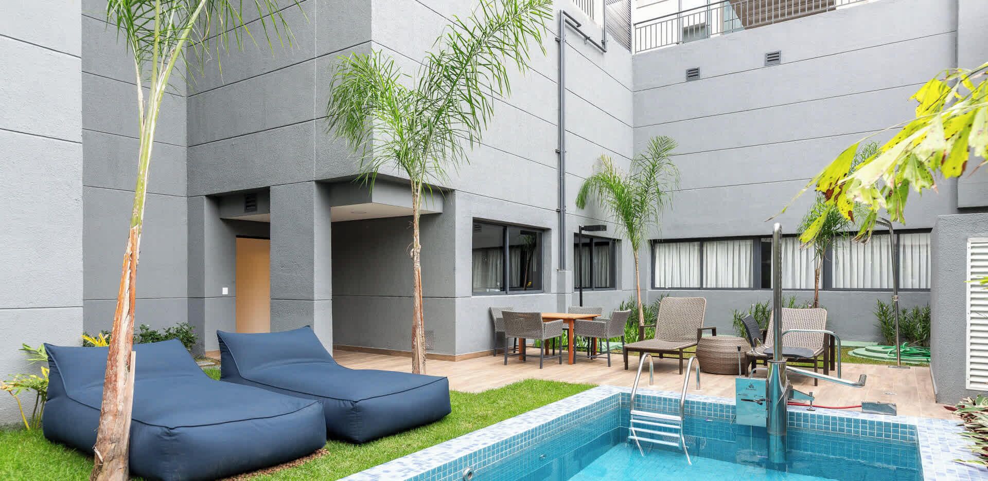 A modern outdoor pool area with lounge seating, a small table, and a poolside bar.