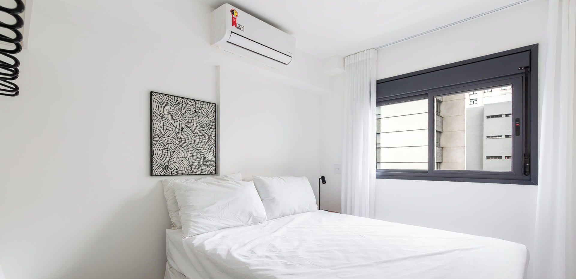 A bedroom with a bed, an air conditioning unit, a window with blinds, and a wall-mounted artwork.