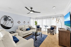A living room with a ceiling fan, a sofa, armchairs, a coffee table, and a TV. - 2bd Condo close to pool and restaurants  (Siesta Key)