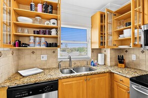 A kitchen with wooden cabinets, granite countertops, a stainless steel sink, and a dishwasher. - 2bd Condo close to pool and restaurants  (Siesta Key)