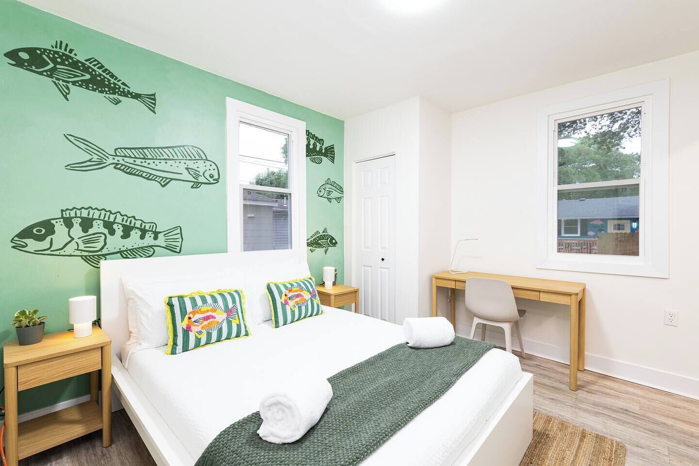 Un dormitorio con cama, escritorio, silla, ventana y decoración en la pared.