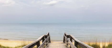 A wooden boardwalk leading to a beach with a calm sea and overcast sky.