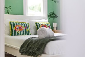 Ein Bett mit zwei Kissen, einem gerollten Handtuch und einer grünen Wand mit einem Fisch-Aufkleber.