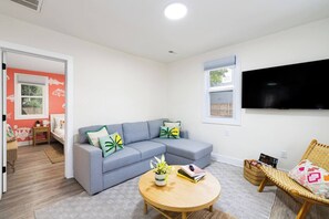 Ein Wohnzimmer mit einem Ecksofa, einem runden Couchtisch, einem Korbstuhl und einem flachbildfernseher, der an der Wand montiert ist.
