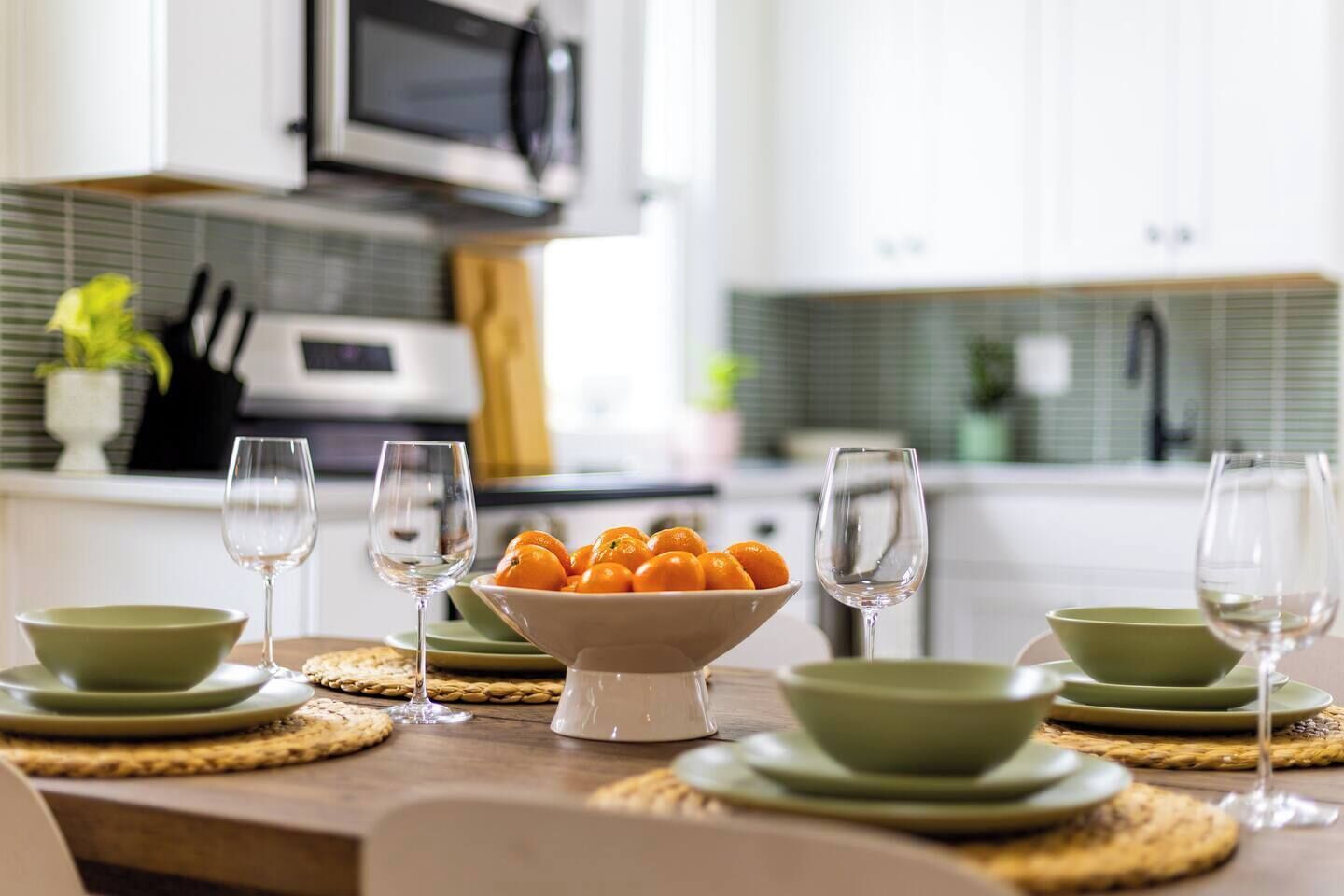 Een eettafel gedekt met groene borden, kommen en wijnglazen, met een schaal mandarijnen in het midden.