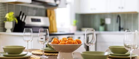 A dining table set with green plates, bowls, and wine glasses, with a bowl of oranges in the center.