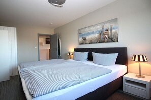 Una habitación de hotel moderna con una cama grande, dos lámparas de noche, un cuadro en la pared y una puerta que da a otra habitación.