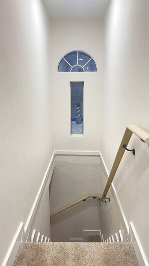 A narrow stairway with a handrail, a small window with a view of a lighthouse, and a white wall. - Game Room, Fire Pit & Fenced Yard · Sleeps 6 (Norfolk)