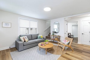 A modern living room with a grey sofa, a round coffee table, and a wicker chair. - Game Room, Fire Pit & Fenced Yard · Sleeps 6 (Norfolk)