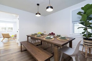 Espaço de refeições com mesa de madeira posta para seis pessoas, duas luminárias pendentes e uma grande planta em vaso.
