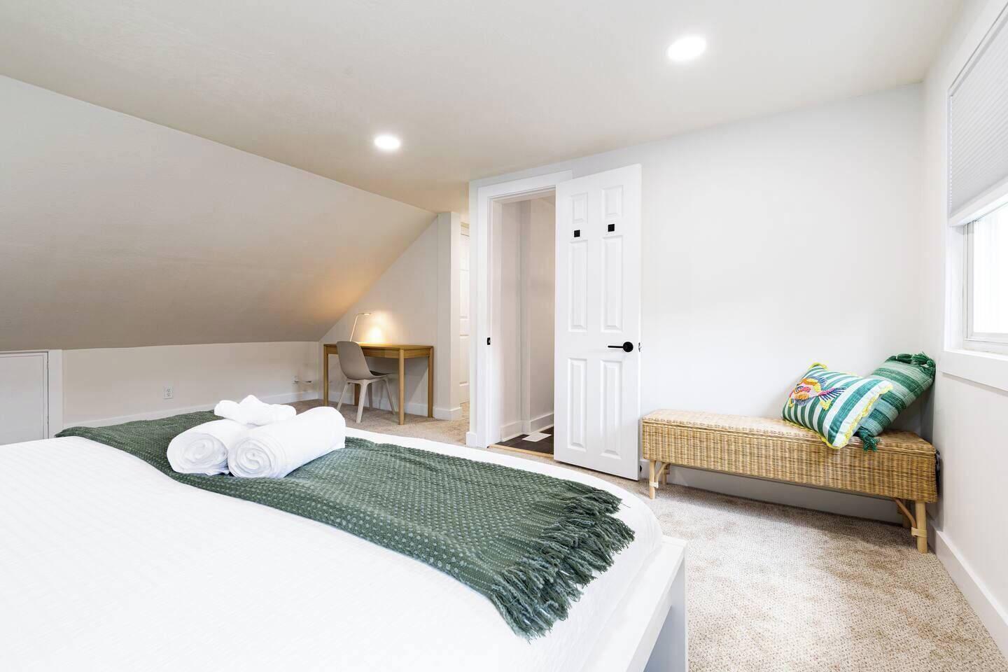 A bedroom with a bed, a desk, a chair, a bench, and a door.