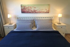 Una cama con almohadones a rayas, un cabecero blanco y dos mesitas de noche con lámparas.