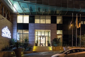 A hotel entrance with a glass facade, a neon sign, and a car parked in front. - NEWDAY (HUSSEIN DEY)