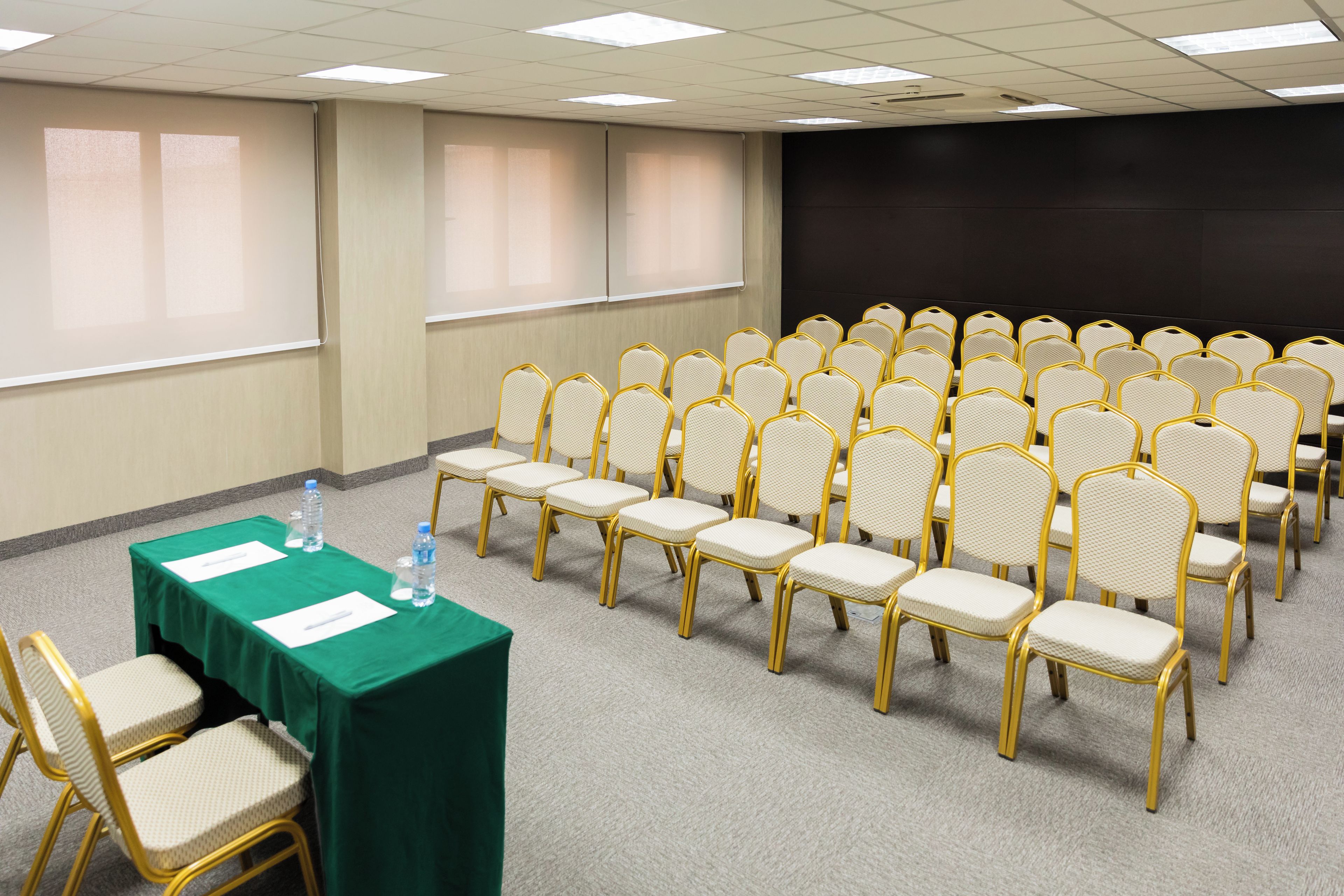 A conference room with rows of chairs, a table with a green tablecloth, and a projector screen.