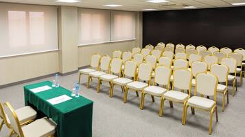 A conference room with rows of chairs, a table with a green tablecloth, and a projector screen.