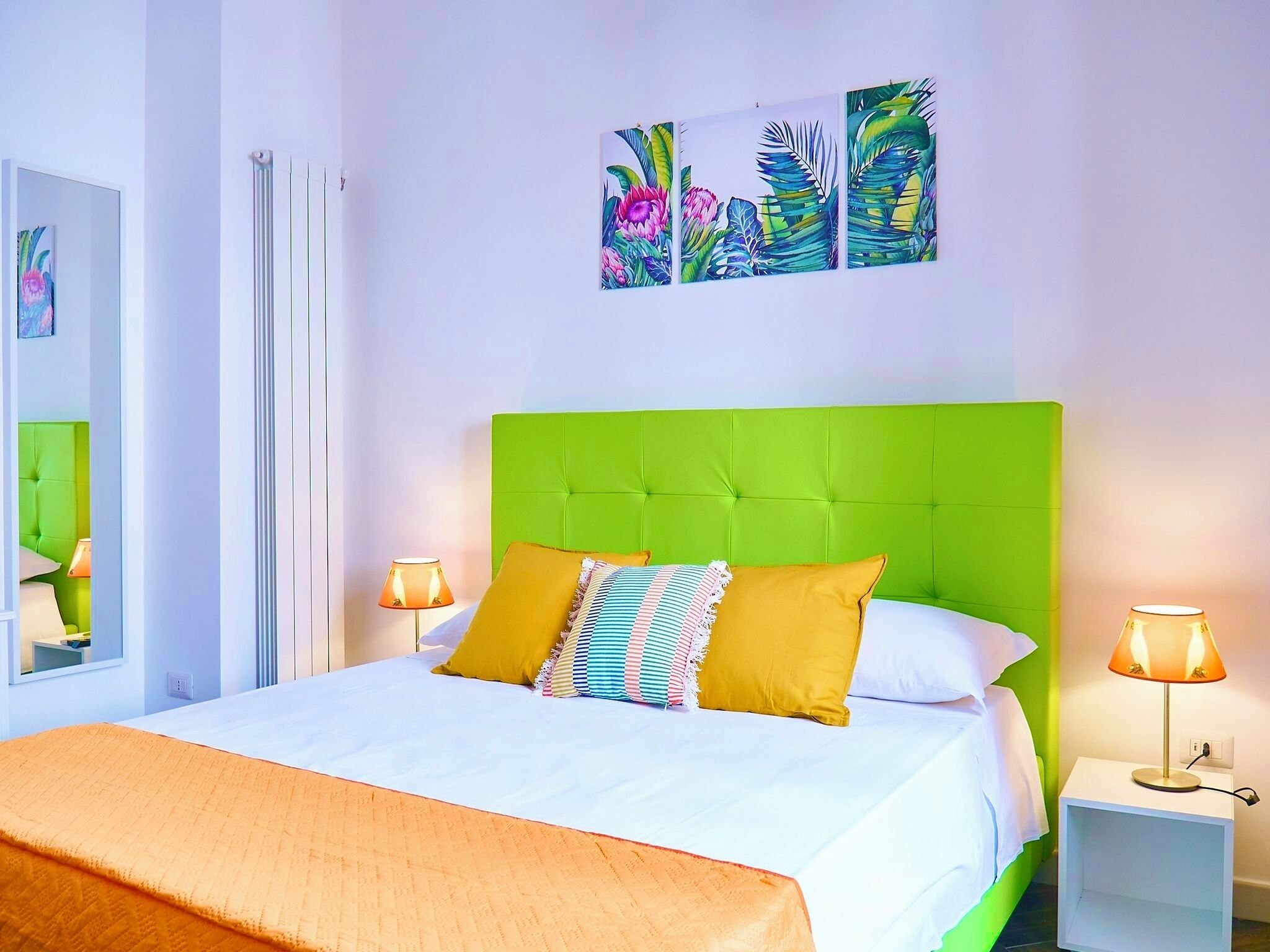 A hotel room with a green upholstered headboard, a large bed with white bedding, two bedside lamps, and a window with a view.