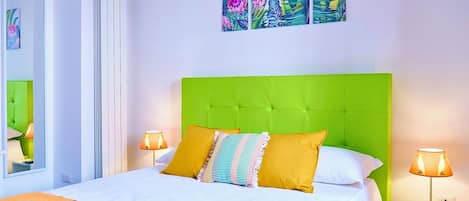 A hotel room with a green upholstered headboard, a large bed with white bedding, two bedside lamps, and a window with a view.