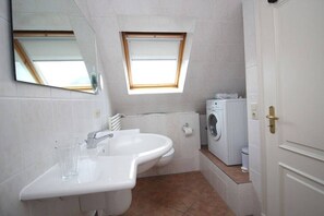 Un baño pequeño con lavamanos, espejo, ventana y lavadora.
