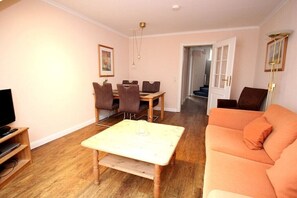 Una sala de estar con una mesa de centro de madera, un sofá, una mesa de comedor con sillas y un televisor sobre un mueble.