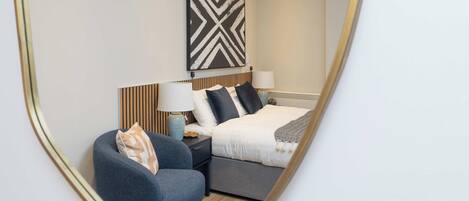 A modern hotel room with a bed, bedside tables, a chair, and a large wall art piece.
