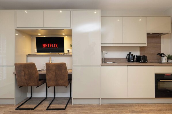 Une cuisine moderne dotée d’un téléviseur encastré affichant le logo « NETFLIX » et d’un coin repas avec deux chaises.