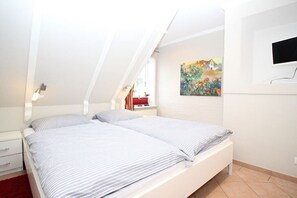 Un dormitorio con techo inclinado, una cama con ropa de cama a rayas, una mesita de noche con una lámpara y un cuadro en la pared.