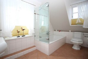 Un baño con ducha envuelta en vidrio, bañera, inodoro y ventana con cortina.