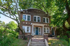 A two-story brick house with a front porch, a front door, and a small attached garage. - Spacious Highland Park Haven (Birmingham)