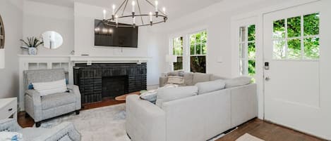 A living room with a fireplace, a sofa, a chair, and a television mounted on the wall.