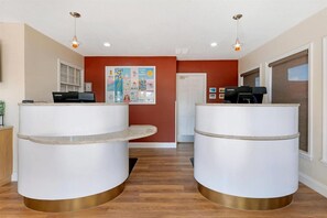 A reception area with two white reception desks, a red wall with a poster, and a wooden floor. - Orlando | Family Theme Park Retreat | Pool + Hot Tub | 2BR (Orlando)