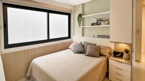 A bedroom with a bed, a window, a shelf with books, and a small plant. - Vrbo Property (Rio de Janeiro)