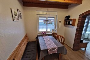 Een eetruimte met een tafel bedekt met een kleed, een bank en een raam met uitzicht.