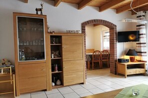 A room with a wooden cabinet, a television, a dining table with chairs, and a brick archway. - Holiday home with 3 bedrooms (Wangerland)