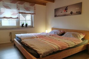 Een kamer met een groot bed, een raam met gordijnen, een radiator en een schilderij aan de muur.