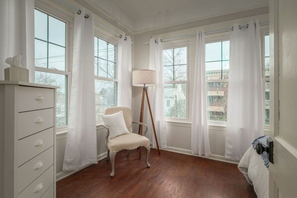 A room with a wooden floor, a white chair, a lamp, and a dresser. - Historic Highland Park Gem (Birmingham)