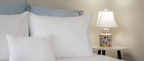 A bed with white bedding and pillows, a round table with a lamp, and a wall with a textured pattern.