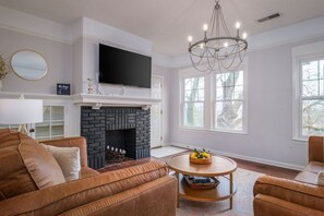 A living room with a fireplace, a television, and a chandelier.