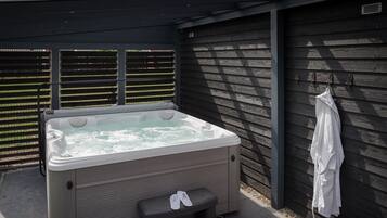 A hot tub with a bench and a pair of slippers, a towel rack, and a wooden fence in the background.