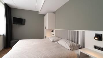 A modern bedroom with a large bed, a flat-screen TV mounted on the wall, a bedside table with a lamp, and a built-in headboard with vertical slats.