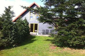 Una casa con techo inclinado, una puerta visible y un pequeño patio con muebles de exterior.