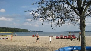 A beach with a volleyball net, a tree, and a blue play structure. - Holiday home with 4 bedrooms (Barderup-Oeversee)
