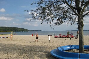 Una playa con una red de voleibol, un árbol y una estructura de juego azul.