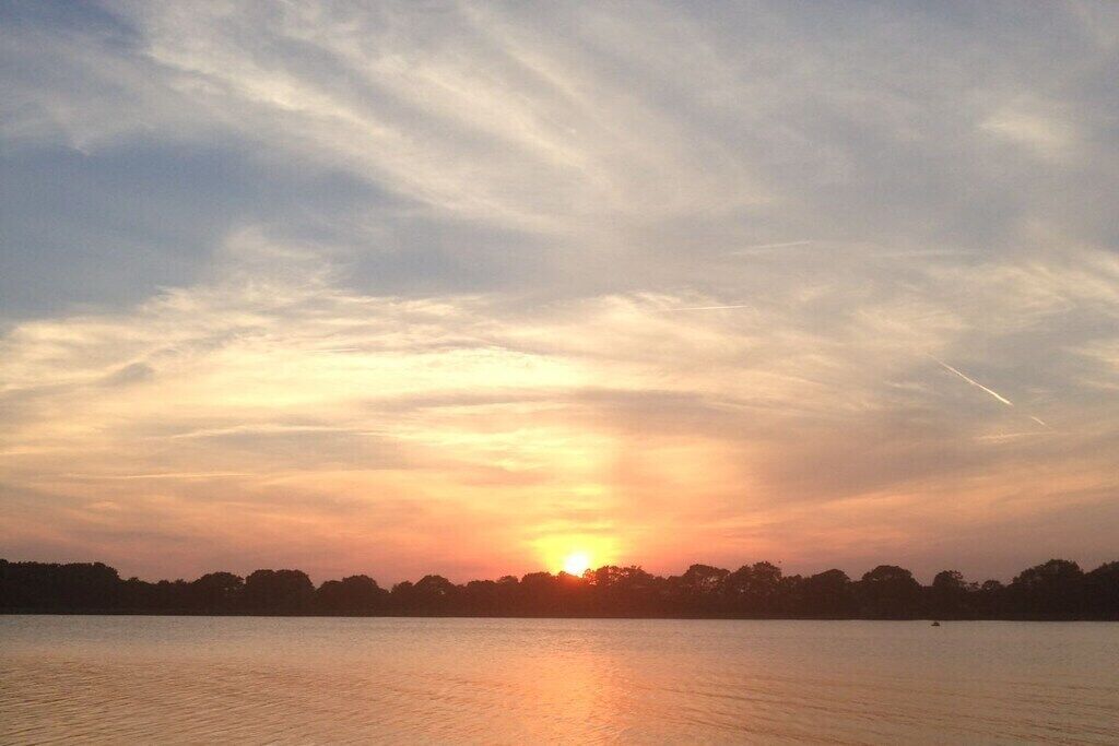 Un atardecer sobre un cuerpo de agua con horizonte despejado y una línea de árboles.