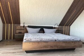 A modern bedroom with a sloped ceiling, a wooden bed frame, and a nightstand with a lamp. - Holiday apartment with 3 bedrooms (Wittdün)