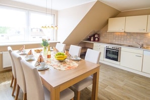 A modern kitchen with a dining area, featuring a wooden table, chairs, and a view of the outdoors. - Holiday apartment with 3 bedrooms (Wittdün)
