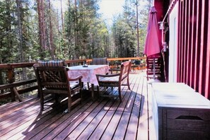 Una terrassa de fusta amb taula i cadires, envoltada per un bosc.