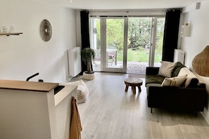 Ein modernes Wohnzimmer mit einer Couch, einem Couchtisch und einer Pflanze. Eine Glastür öffnet sich zu einer Terrasse mit Gartenmöbeln.