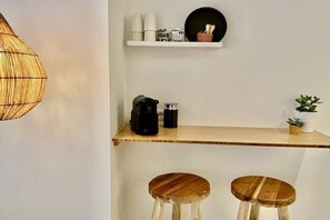 Ein Küchenbereich mit Holztischplatte, zwei Barhocker, einer Pendelleuchte und einem Regal mit Küchenutensilien.