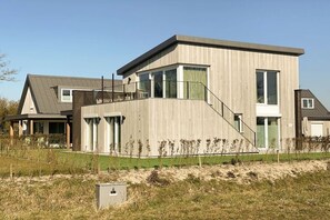 A modern two-story house with a flat roof, large windows, and a visible staircase leading to the upper floor. - Villa in Kamperland with barbecue (Kamperland)