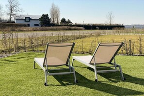 Two outdoor lounge chairs on a well-maintained lawn with a view of a body of water and a building in the background. - Villa in Kamperland with barbecue (Kamperland)